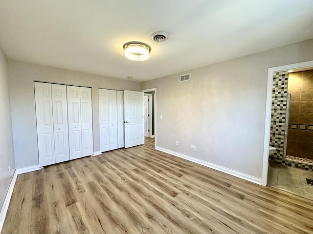 unfurnished bedroom featuring multiple closets, visible vents, baseboards, and wood finished floors