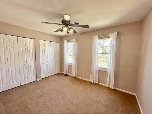 unfurnished bedroom with carpet, multiple windows, baseboards, and multiple closets