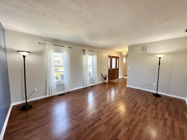 unfurnished living room with dark wood-style flooring, visible vents, and baseboards