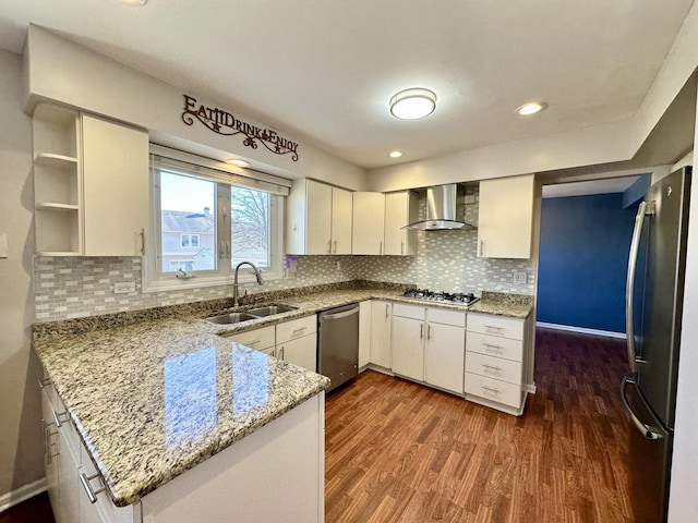 kitchen with a peninsula, a sink, wall chimney range hood, appliances with stainless steel finishes, and dark wood-style floors