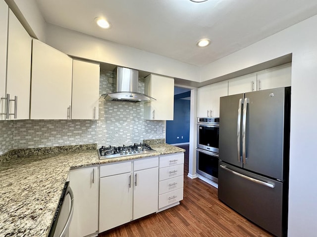 kitchen with white cabinets, appliances with stainless steel finishes, wall chimney exhaust hood, tasteful backsplash, and dark wood finished floors