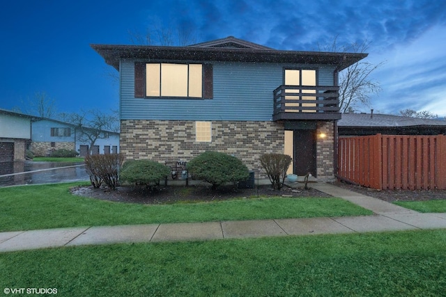 view of front of house with a balcony, fence, a front lawn, and brick siding