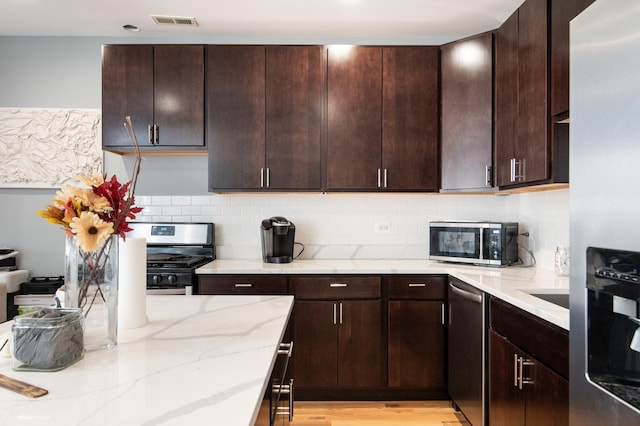 kitchen with light wood finished floors, visible vents, appliances with stainless steel finishes, light stone countertops, and backsplash