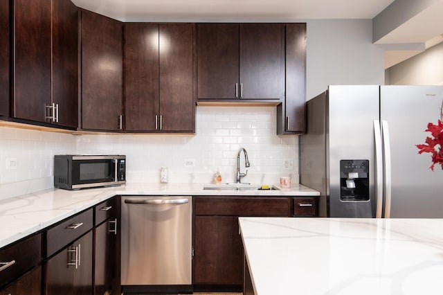 kitchen featuring light stone counters, appliances with stainless steel finishes, decorative backsplash, and a sink