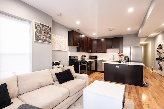 kitchen featuring a kitchen island, open floor plan, dark brown cabinets, appliances with stainless steel finishes, and light countertops