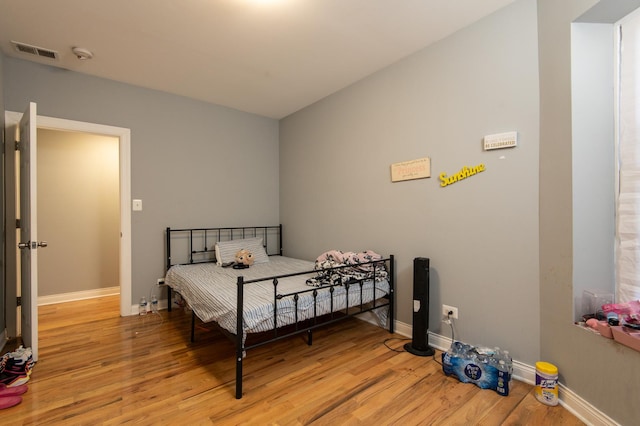 bedroom with baseboards, visible vents, and wood finished floors