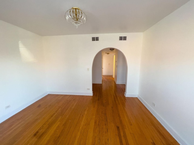 empty room featuring arched walkways, wood finished floors, visible vents, and baseboards