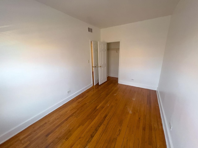 empty room featuring hardwood / wood-style flooring, visible vents, and baseboards