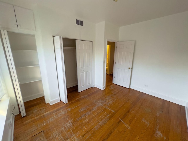 unfurnished bedroom with wood-type flooring, visible vents, baseboards, and a closet