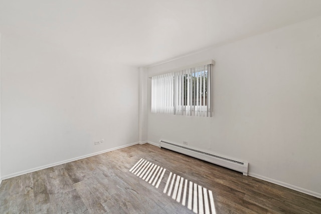 unfurnished room featuring a baseboard radiator, baseboards, and wood finished floors