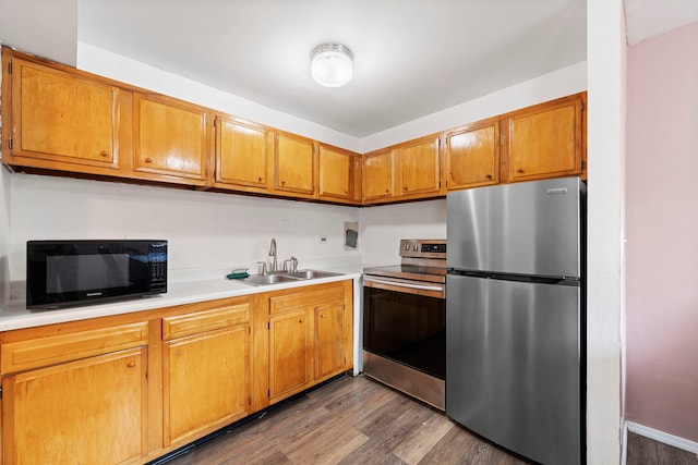 kitchen with appliances with stainless steel finishes, brown cabinets, wood finished floors, light countertops, and a sink