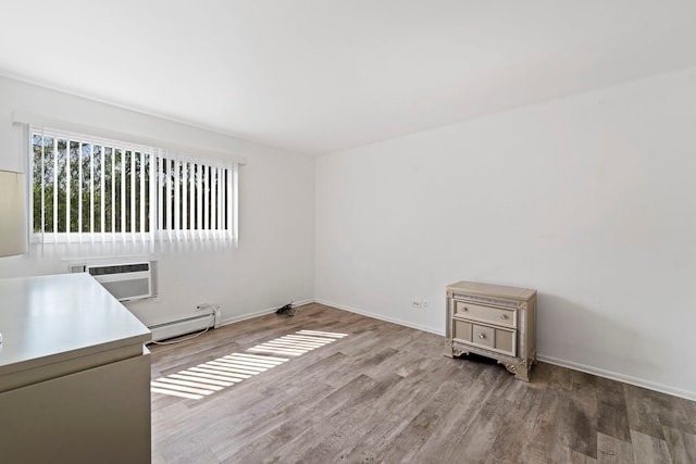 empty room with a baseboard heating unit, a wall unit AC, wood finished floors, and baseboards