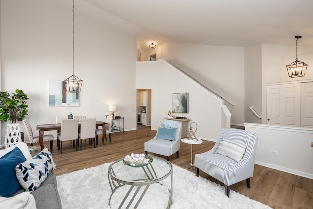 living area featuring high vaulted ceiling, wood finished floors, stairway, an inviting chandelier, and baseboards