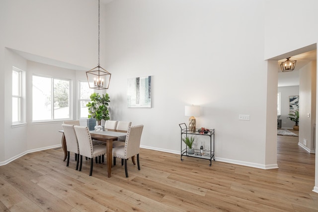 dining space with a high ceiling, a notable chandelier, wood finished floors, and baseboards