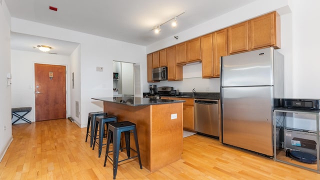 kitchen with a sink, a kitchen island, appliances with stainless steel finishes, and light wood finished floors