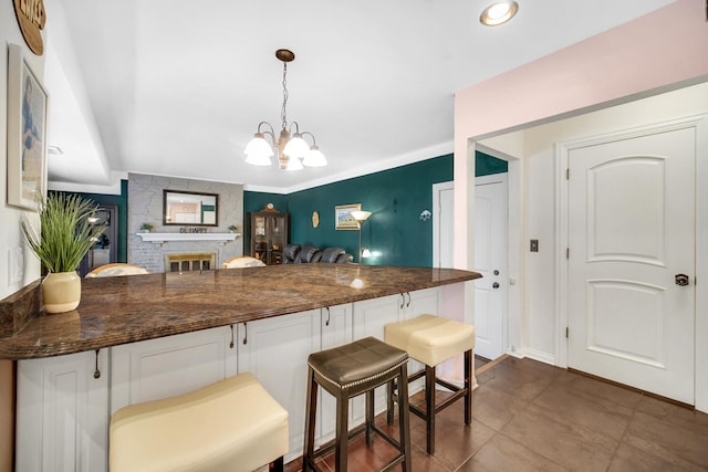 kitchen with dark stone counters, a kitchen breakfast bar, decorative light fixtures, a fireplace, and a notable chandelier