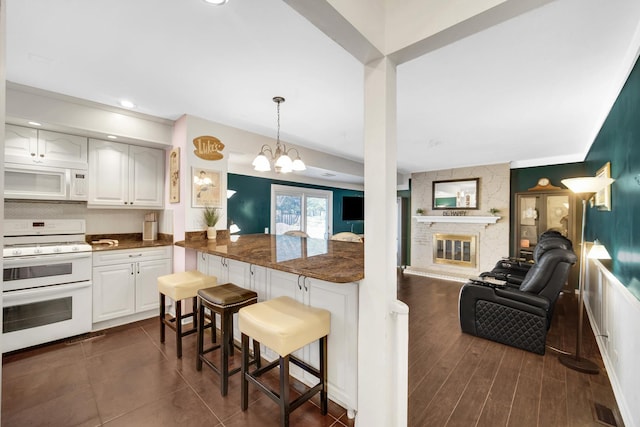 kitchen with white appliances, decorative backsplash, a kitchen breakfast bar, open floor plan, and a fireplace