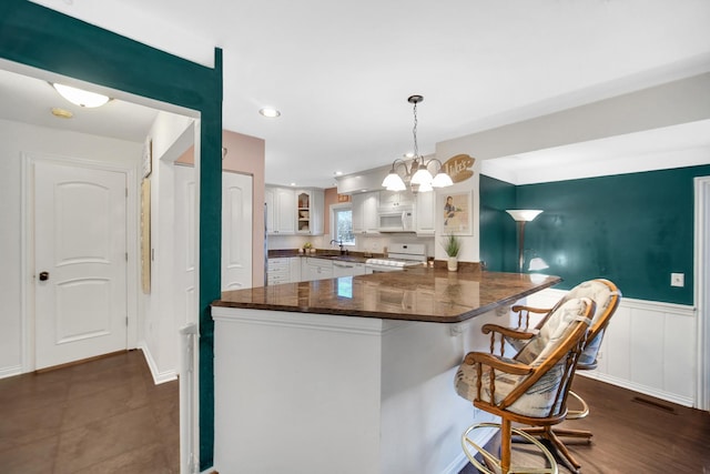 kitchen with white appliances, white cabinets, dark countertops, a breakfast bar area, and a peninsula