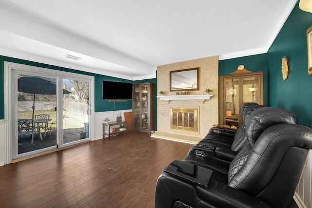 living room featuring a wainscoted wall, a fireplace, wood finished floors, visible vents, and crown molding