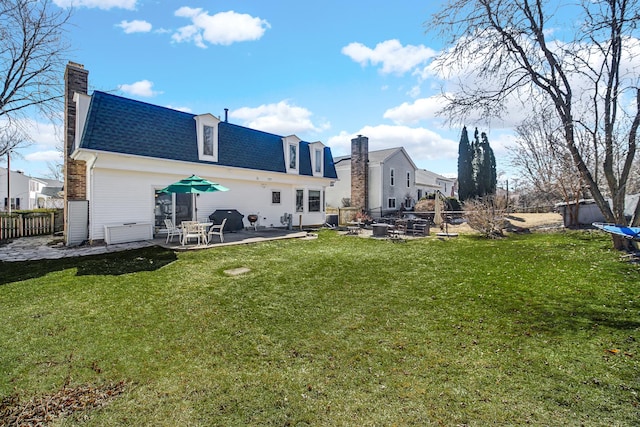 rear view of property with mansard roof, a shingled roof, a lawn, a patio area, and fence