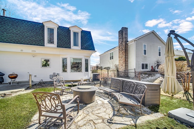 rear view of property featuring a patio, mansard roof, a fire pit, fence, and roof with shingles