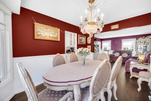 dining space with dark wood-style flooring, wainscoting, and an inviting chandelier