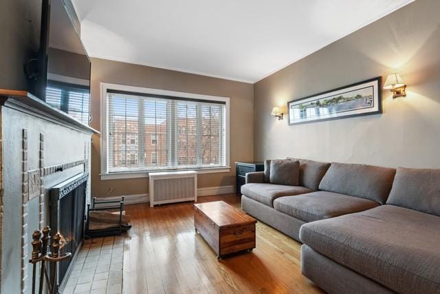 living room with radiator heating unit, a fireplace, baseboards, and wood finished floors