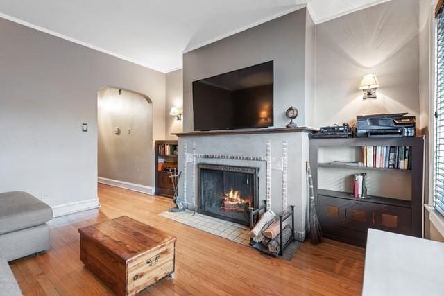 living room featuring arched walkways, a tiled fireplace, wood finished floors, and baseboards