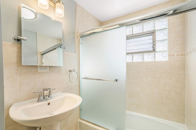 full bathroom featuring tile walls, combined bath / shower with glass door, and a sink