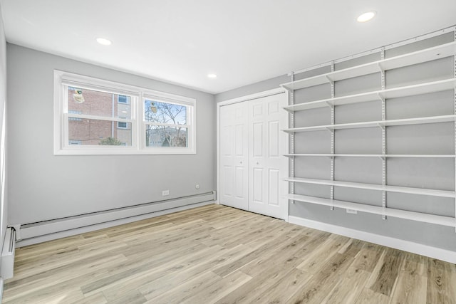 unfurnished bedroom with recessed lighting, a closet, baseboard heating, and wood finished floors