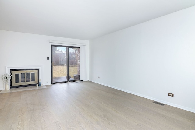 unfurnished living room with a fireplace with flush hearth, wood finished floors, visible vents, and baseboards