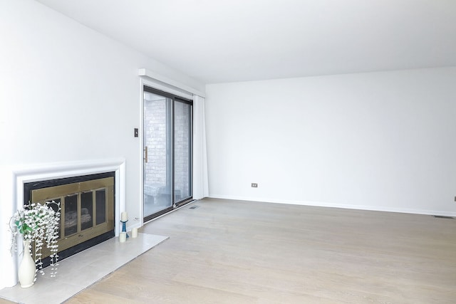 unfurnished living room featuring baseboards, wood finished floors, and a glass covered fireplace