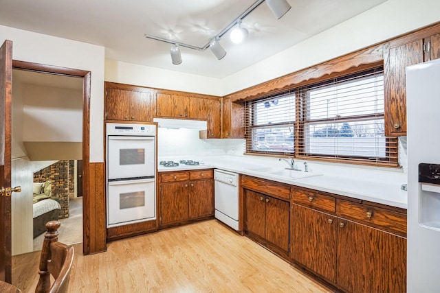 kitchen featuring white appliances, light wood finished floors, light countertops, under cabinet range hood, and a sink