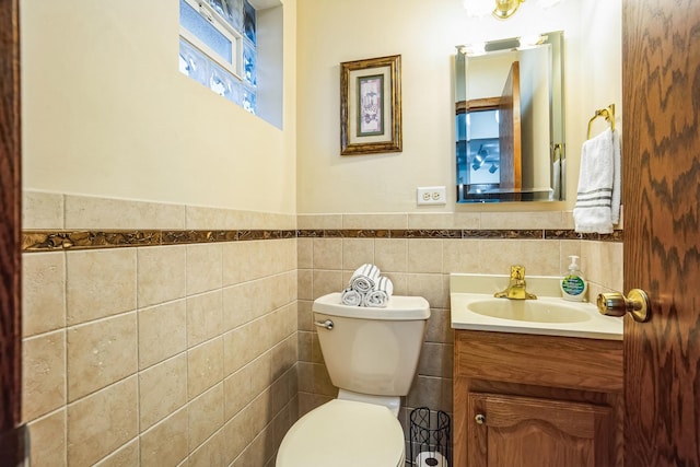 half bathroom with a wainscoted wall, vanity, toilet, and tile walls