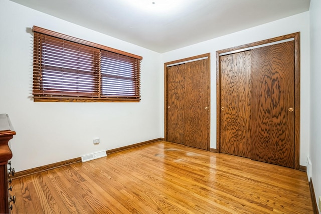 unfurnished bedroom with baseboards, light wood-style flooring, visible vents, and two closets