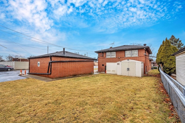 rear view of property featuring brick siding, fence, an outbuilding, and a yard