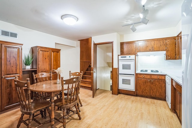 kitchen with white appliances, visible vents, brown cabinetry, light wood-style flooring, and under cabinet range hood