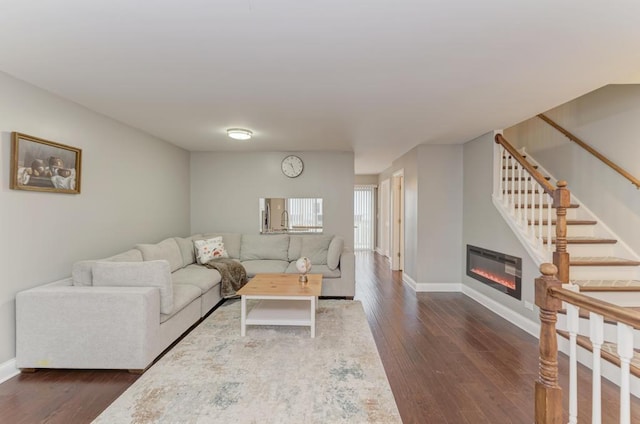 living area featuring stairs, a glass covered fireplace, baseboards, and dark wood-style flooring