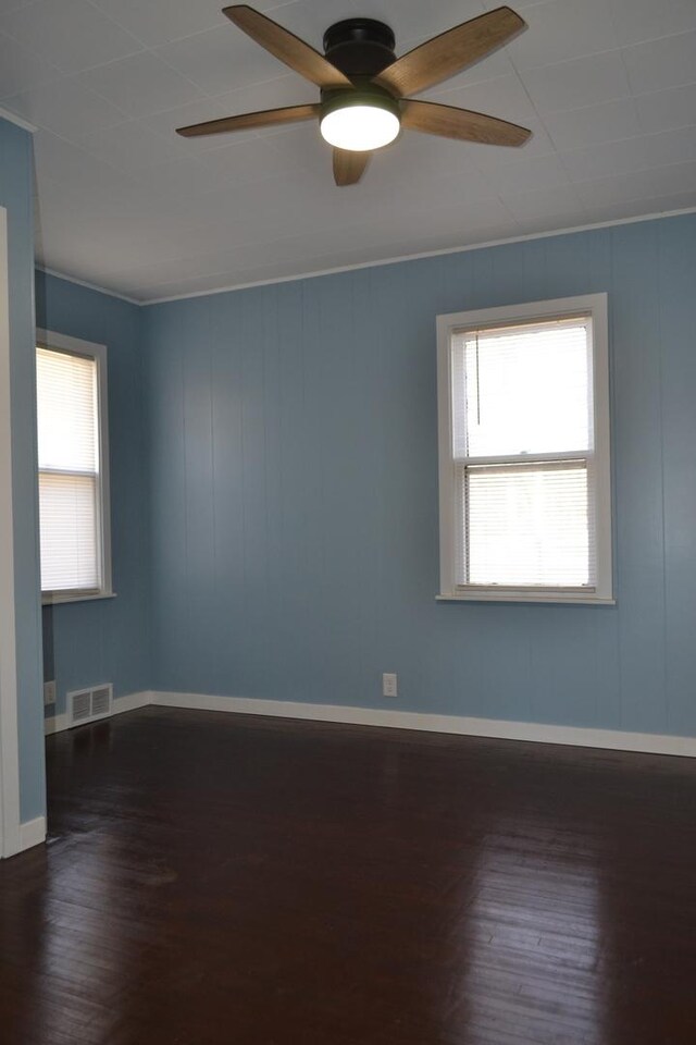 spare room with a ceiling fan, visible vents, baseboards, and wood finished floors