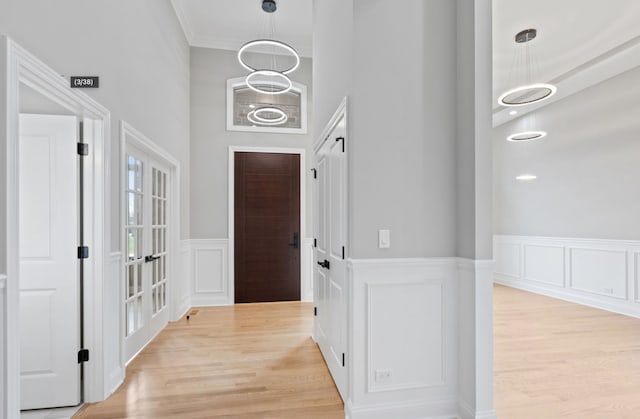 entrance foyer featuring crown molding, light wood finished floors, wainscoting, and a decorative wall