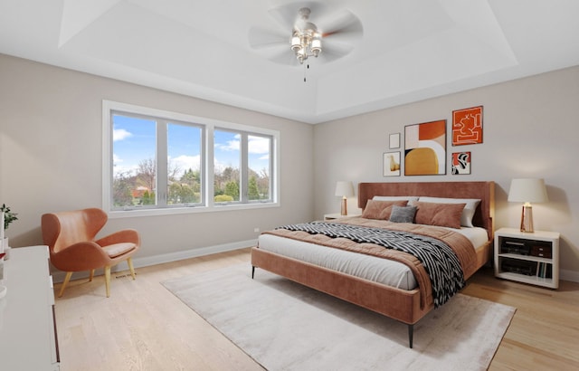 bedroom featuring a tray ceiling, ceiling fan, light wood-style flooring, and baseboards