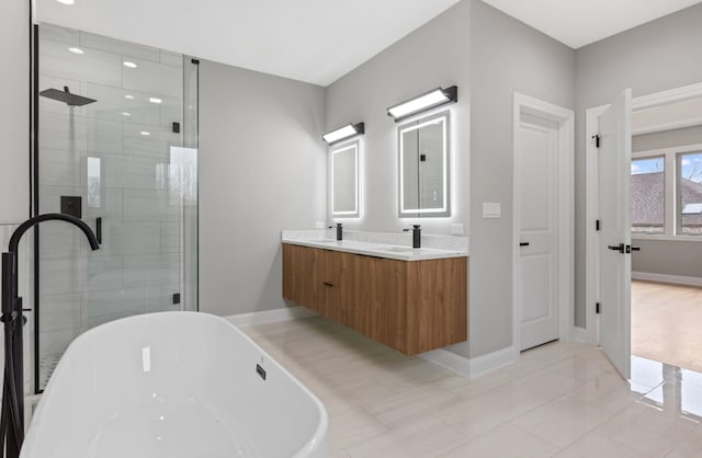 full bath with double vanity, a freestanding tub, a shower stall, and baseboards