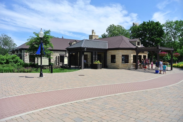 exterior space with metal roof, stone siding, a pergola, a standing seam roof, and a chimney