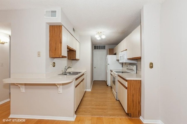 kitchen with a peninsula, white appliances, visible vents, and a sink