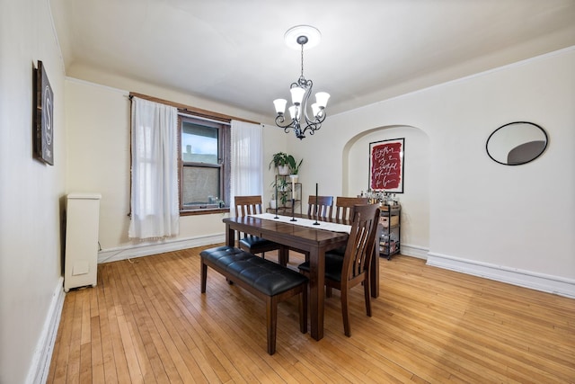 dining space featuring light wood-type flooring, baseboards, arched walkways, and a notable chandelier