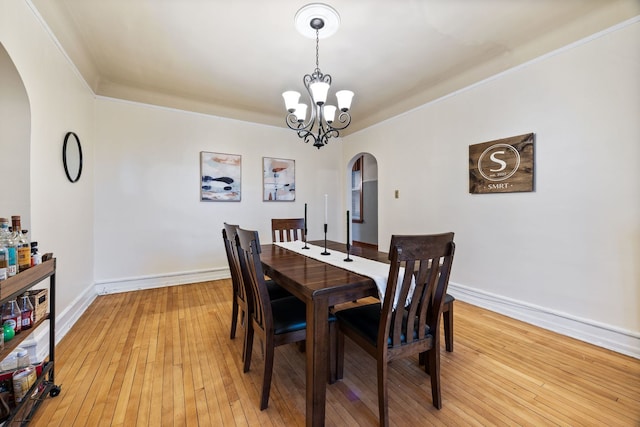 dining space with an inviting chandelier, light wood-style flooring, arched walkways, and baseboards