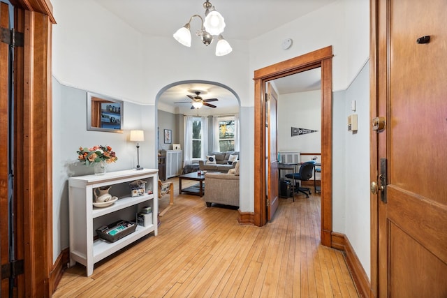 hallway with arched walkways, light wood-type flooring, a chandelier, and baseboards