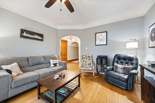 living room with light wood-style floors, a ceiling fan, arched walkways, and crown molding