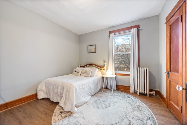 bedroom with baseboards, light wood-style flooring, and radiator heating unit