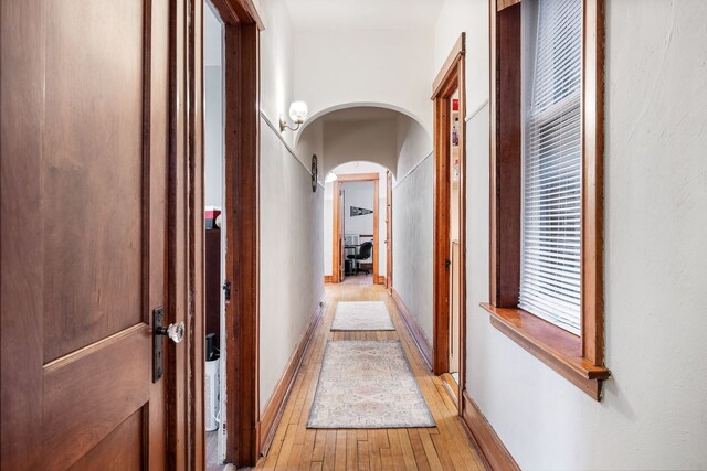 hallway with arched walkways and light wood-type flooring